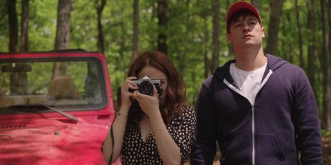 Costume design by Anette Cseri for the film The In Between: a young woman photographing with a film camera beside a young man in a red cap, next to a red jeep in the woods